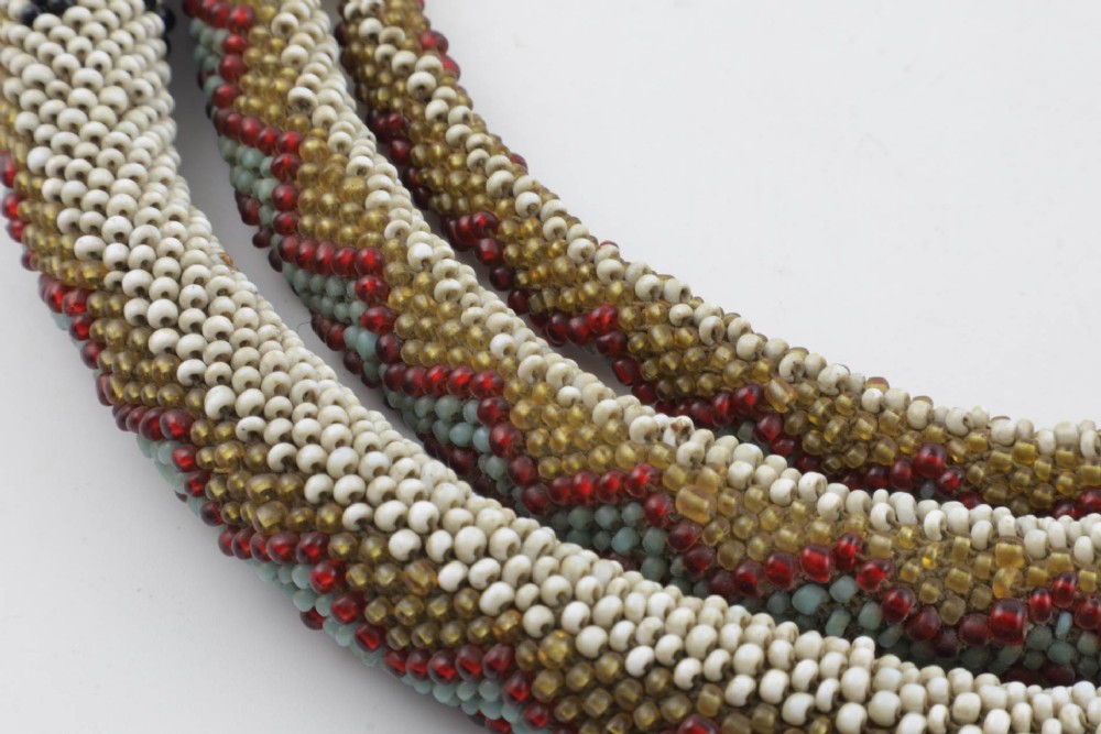 A long, hand-crafted glass beadwork snake with white, olive green, and red geometric patterns coiled into a spiral, featuring text reading TURKISH PRISONERS 1918 woven into its body. View XI