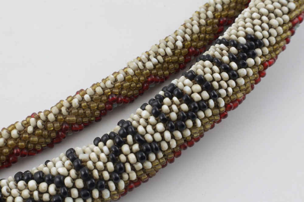 A long, hand-crafted glass beadwork snake with white, olive green, and red geometric patterns coiled into a spiral, featuring text reading TURKISH PRISONERS 1918 woven into its body. View XII