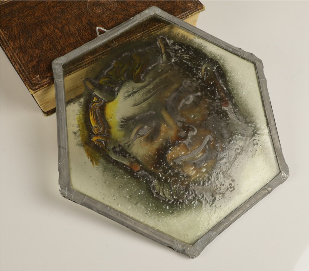 A hexagonal leaded stained glass panel featuring a hand-painted depiction of a horned devil head in grey, black, and amber tones. View III