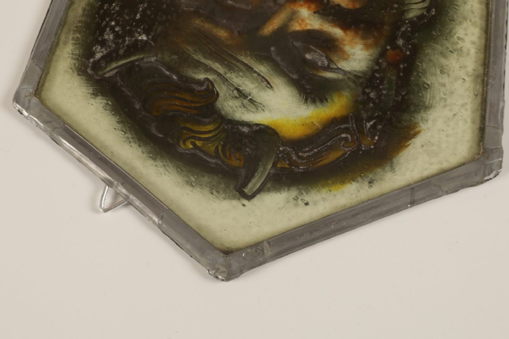 A hexagonal leaded stained glass panel featuring a hand-painted depiction of a horned devil head in grey, black, and amber tones. View VI
