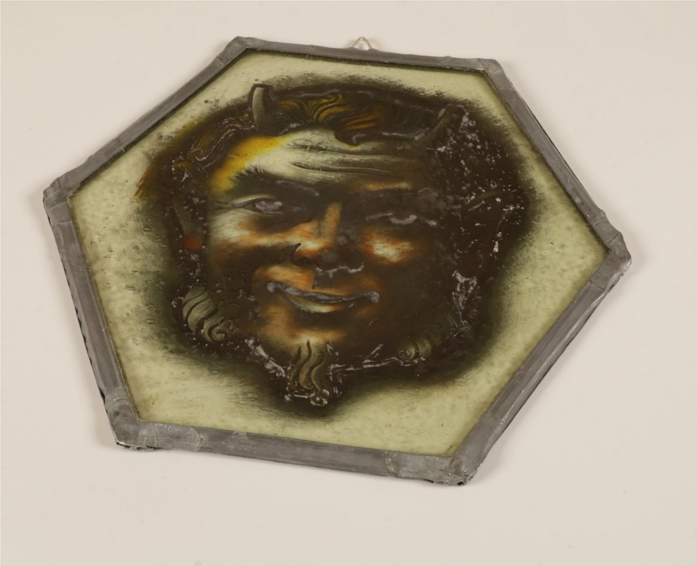 A hexagonal leaded stained glass panel featuring a hand-painted depiction of a horned devil head in grey, black, and amber tones. View XIII