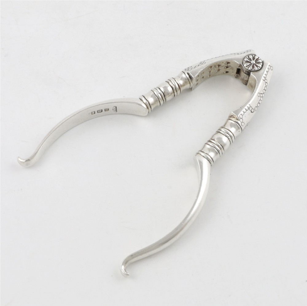 A pair of hallmarked sterling silver nutcrackers with hinged, textured jaws and curved handles featuring decorative chasing. View II