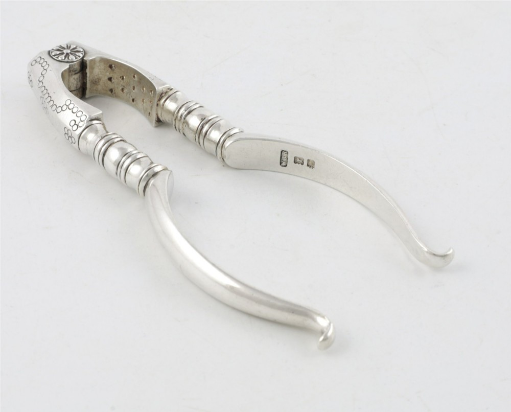 A pair of hallmarked sterling silver nutcrackers with hinged, textured jaws and curved handles featuring decorative chasing. View III