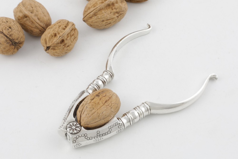 A pair of hallmarked sterling silver nutcrackers with hinged, textured jaws and curved handles featuring decorative chasing. View VI