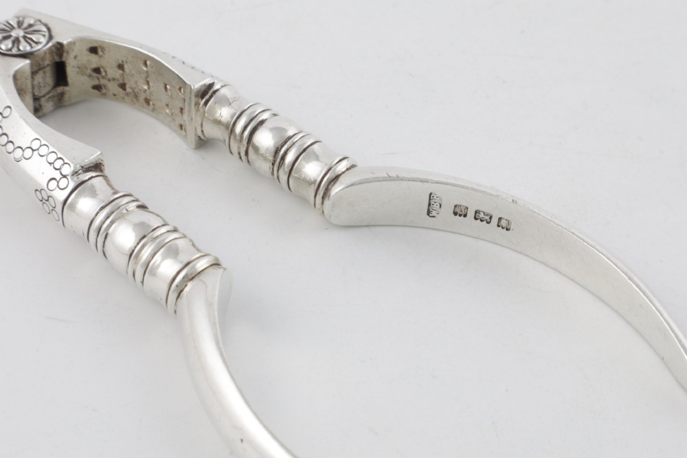 A pair of hallmarked sterling silver nutcrackers with hinged, textured jaws and curved handles featuring decorative chasing. View IX