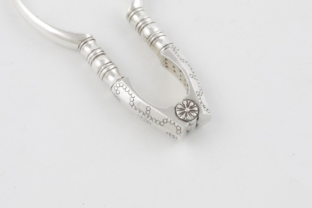 A pair of hallmarked sterling silver nutcrackers with hinged, textured jaws and curved handles featuring decorative chasing. View X