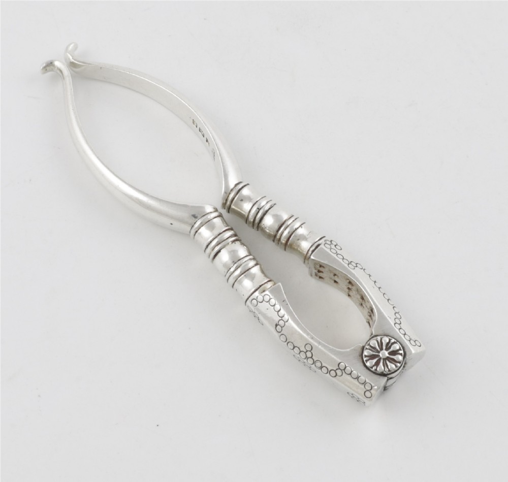 A pair of hallmarked sterling silver nutcrackers with hinged, textured jaws and curved handles featuring decorative chasing. View XI