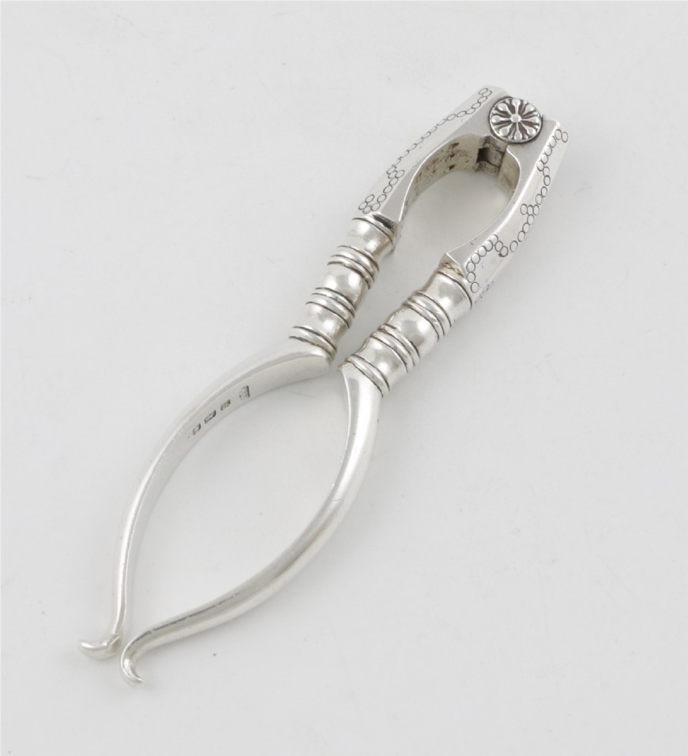 A pair of hallmarked sterling silver nutcrackers with hinged, textured jaws and curved handles featuring decorative chasing. View XIII