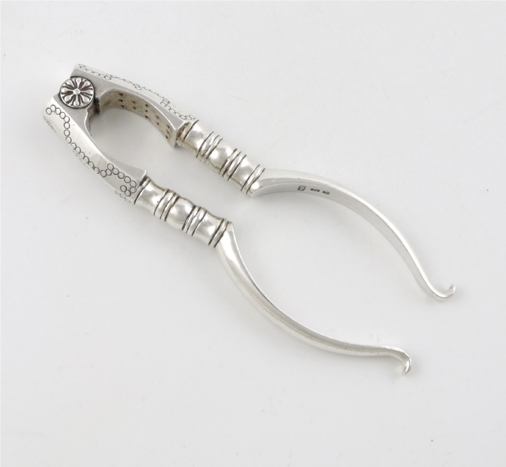 A pair of hallmarked sterling silver nutcrackers with hinged, textured jaws and curved handles featuring decorative chasing. View XV