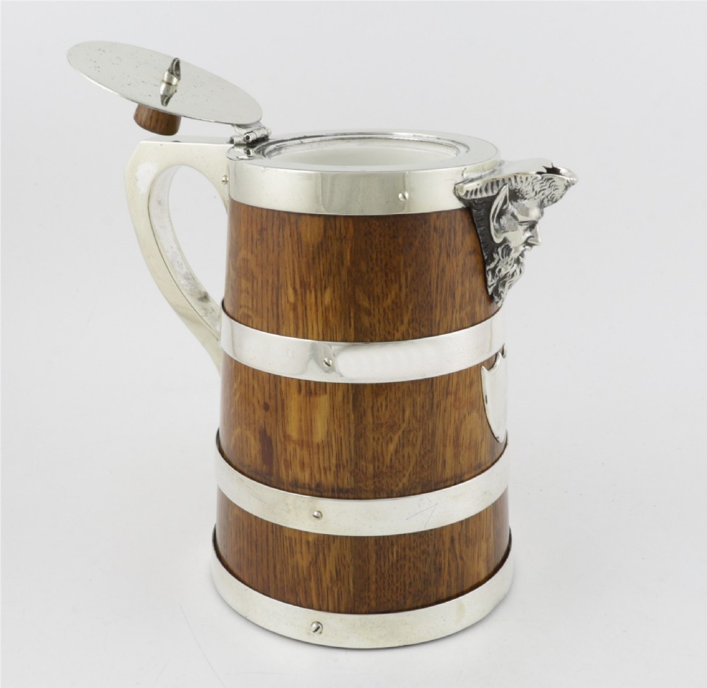 A Victorian coopered oak wine pitcher featuring silver-plated bands, a detailed Bacchus spout, and a hinged lid with a wooden finial. View V