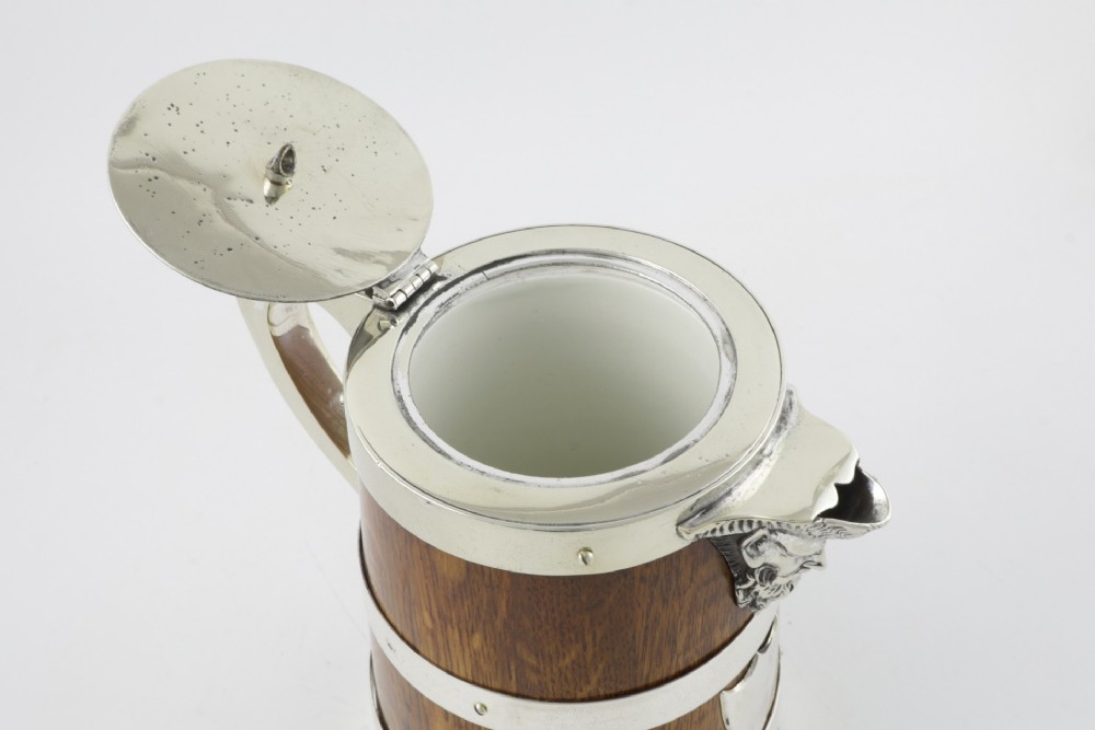 A Victorian coopered oak wine pitcher featuring silver-plated bands, a detailed Bacchus spout, and a hinged lid with a wooden finial. View IX