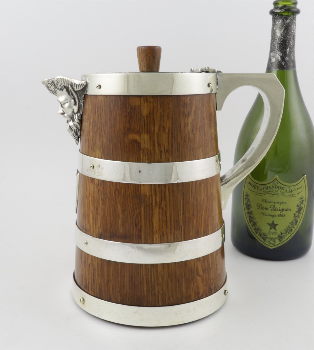 A Victorian coopered oak wine pitcher featuring silver-plated bands, a detailed Bacchus spout, and a hinged lid with a wooden finial. View XII