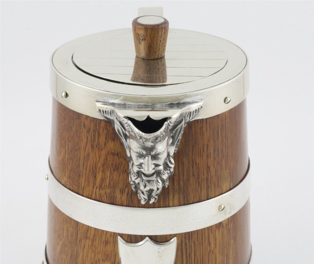 A Victorian coopered oak wine pitcher featuring silver-plated bands, a detailed Bacchus spout, and a hinged lid with a wooden finial. View XIV