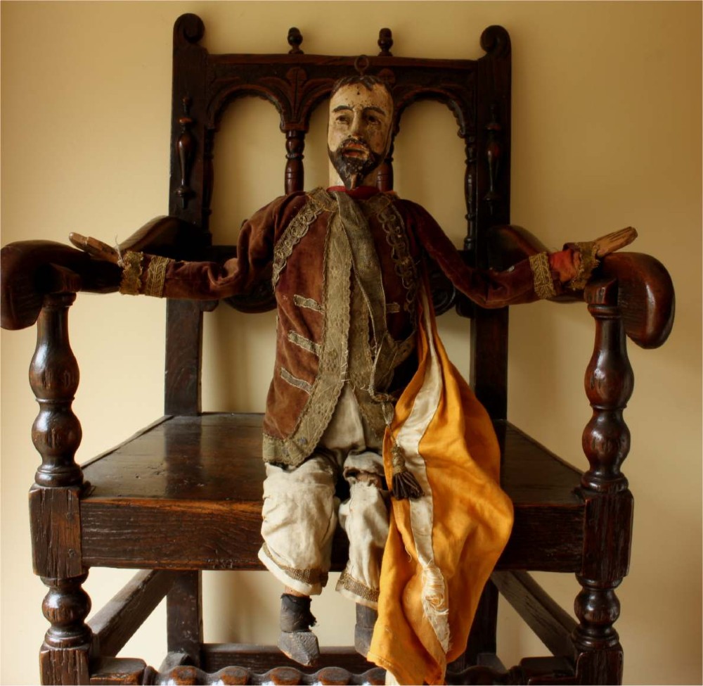An antique French folk art marionette puppet with a hand-carved bearded wooden head, articulated limbs, and a brown velvet jacket trimmed with braid.