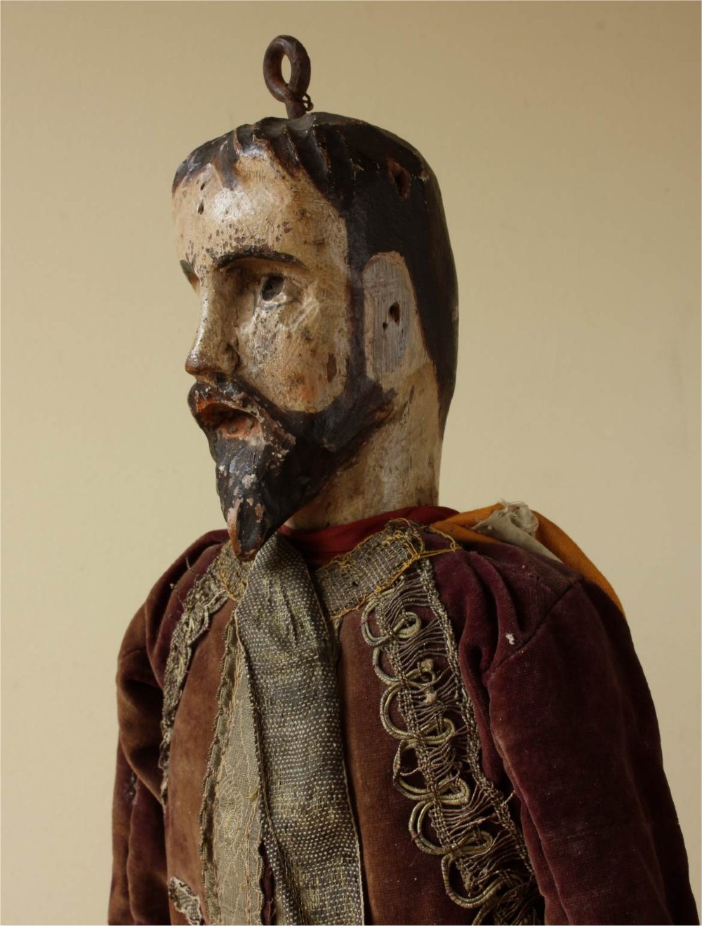 An antique French folk art marionette puppet with a hand-carved bearded wooden head, articulated limbs, and a brown velvet jacket trimmed with braid. View X