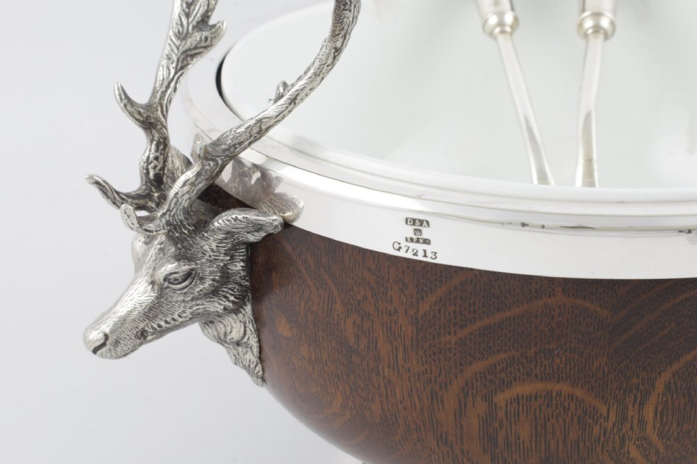 A turned dark oak bowl featuring a silver-plated rim, cast stag head handles, a central vacant silver shield, and matching serving utensils. View III