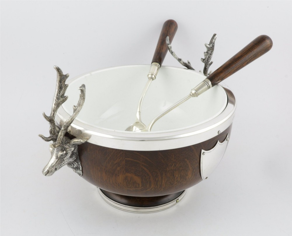 A turned dark oak bowl featuring a silver-plated rim, cast stag head handles, a central vacant silver shield, and matching serving utensils. View VIII
