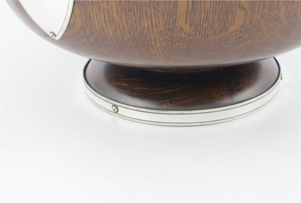 A turned dark oak bowl featuring a silver-plated rim, cast stag head handles, a central vacant silver shield, and matching serving utensils. View XII