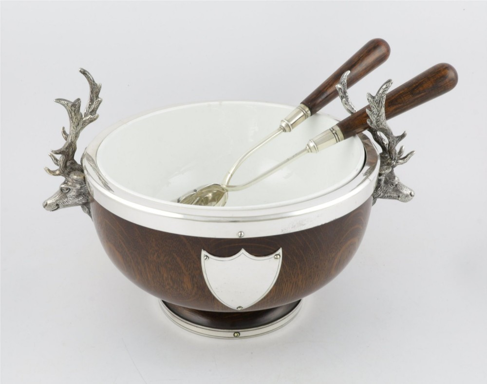 A turned dark oak bowl featuring a silver-plated rim, cast stag head handles, a central vacant silver shield, and matching serving utensils. View XIV