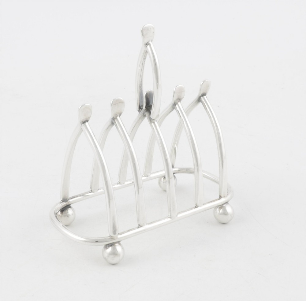 An antique silver-plated wishbone toast rack featuring four divisions and spherical feet against a plain background.