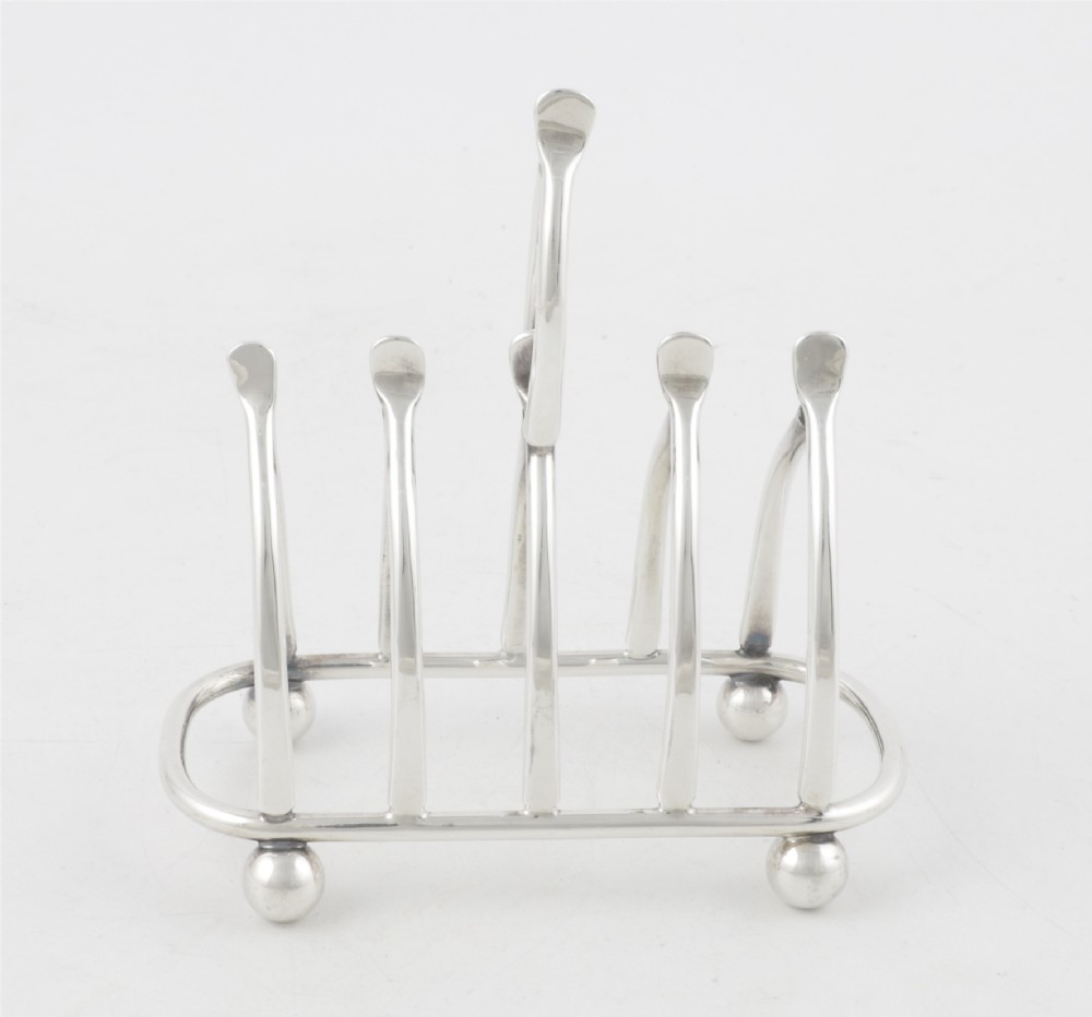 An antique silver-plated wishbone toast rack featuring four divisions and spherical feet against a plain background. View II
