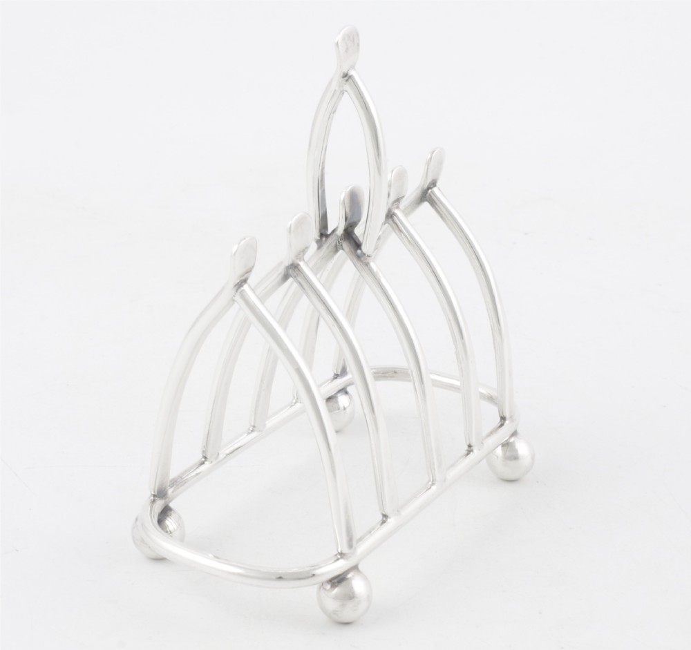 An antique silver-plated wishbone toast rack featuring four divisions and spherical feet against a plain background. View III