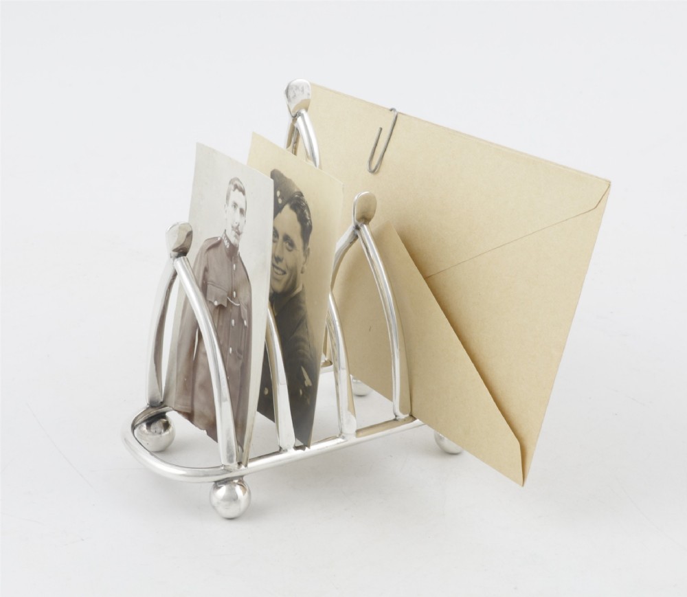 An antique silver-plated wishbone toast rack featuring four divisions and spherical feet against a plain background. View IV