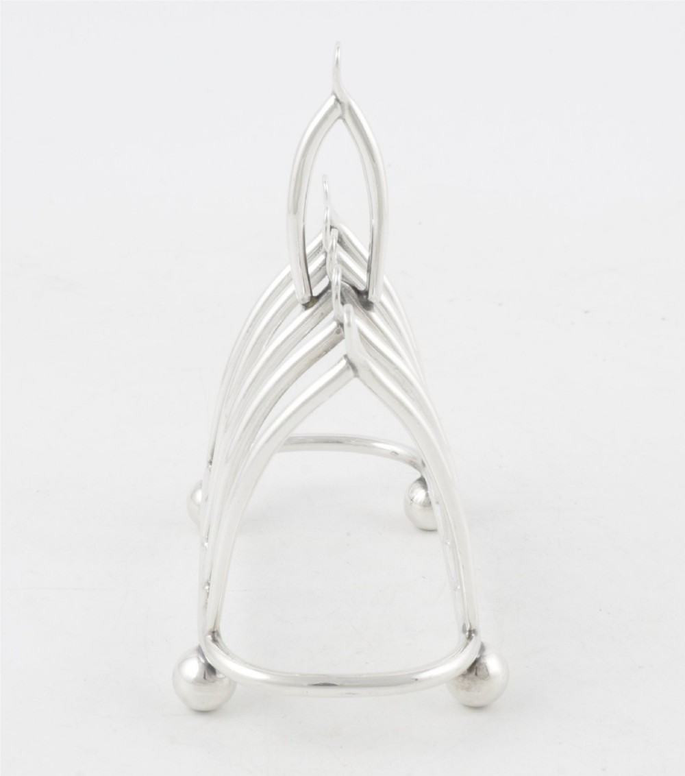 An antique silver-plated wishbone toast rack featuring four divisions and spherical feet against a plain background. View V