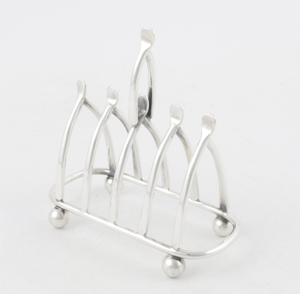 An antique silver-plated wishbone toast rack featuring four divisions and spherical feet against a plain background. View VI