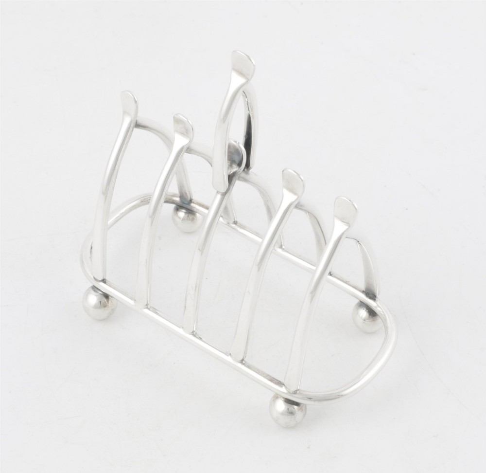 An antique silver-plated wishbone toast rack featuring four divisions and spherical feet against a plain background. View VII