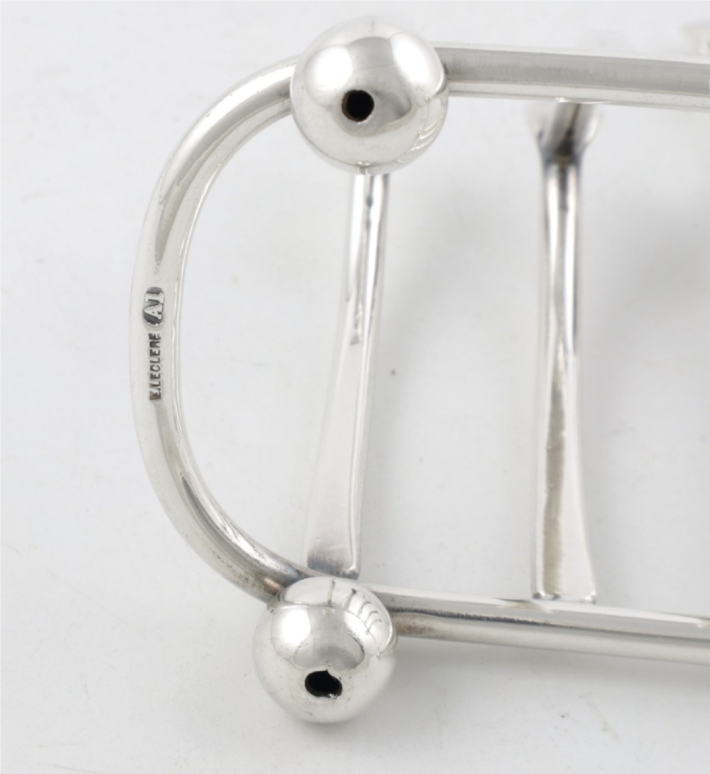 An antique silver-plated wishbone toast rack featuring four divisions and spherical feet against a plain background. View VIII