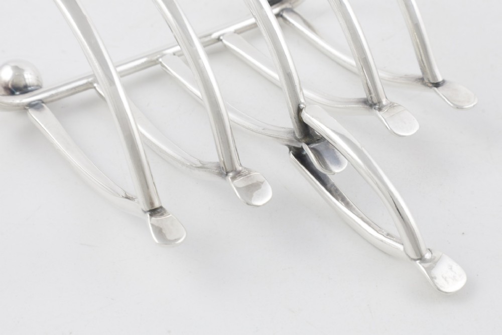An antique silver-plated wishbone toast rack featuring four divisions and spherical feet against a plain background. View IX