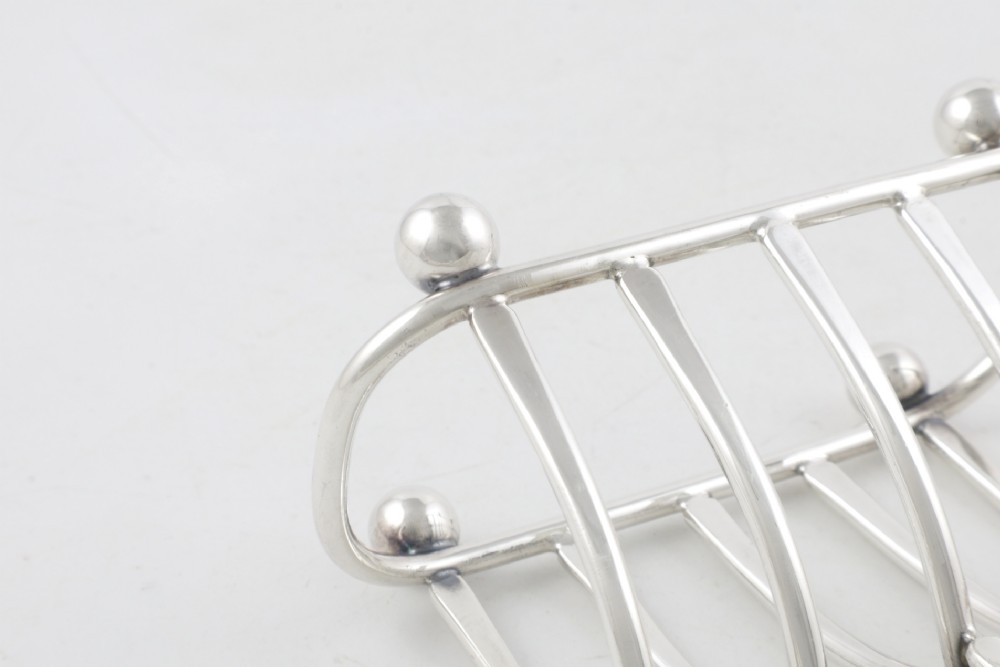 An antique silver-plated wishbone toast rack featuring four divisions and spherical feet against a plain background. View X