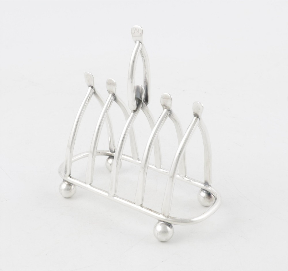 An antique silver-plated wishbone toast rack featuring four divisions and spherical feet against a plain background. View XI