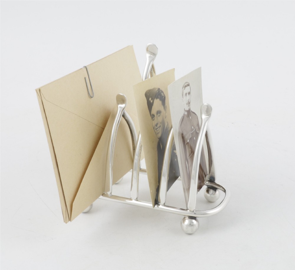 An antique silver-plated wishbone toast rack featuring four divisions and spherical feet against a plain background. View XII