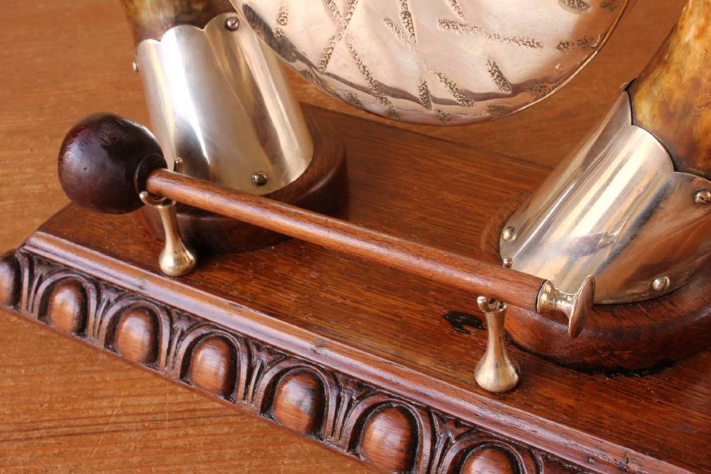 A Victorian dinner gong featuring a hammered silver-plated disc suspended between two curved bovine horns mounted on a carved oak base with a striker. View V