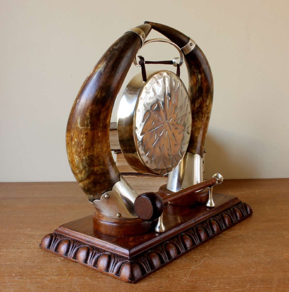 A Victorian dinner gong featuring a hammered silver-plated disc suspended between two curved bovine horns mounted on a carved oak base with a striker. View VI