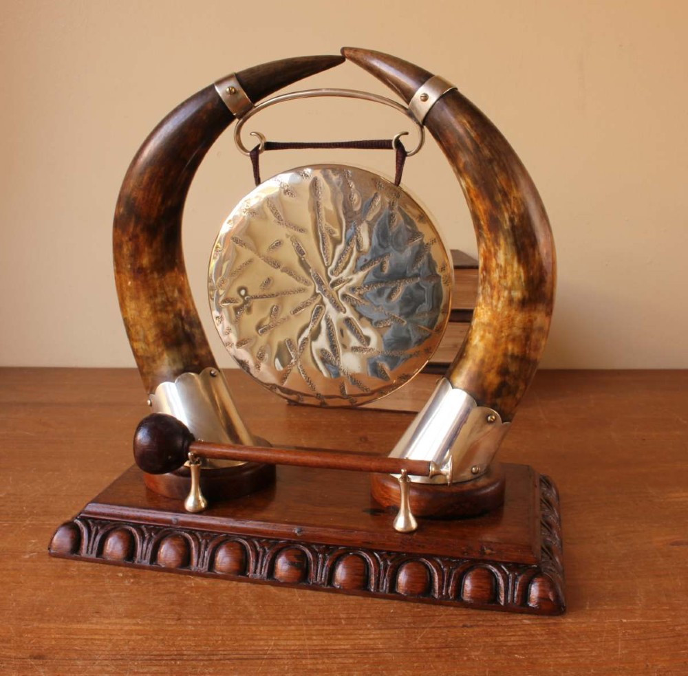A Victorian dinner gong featuring a hammered silver-plated disc suspended between two curved bovine horns mounted on a carved oak base with a striker. View VII