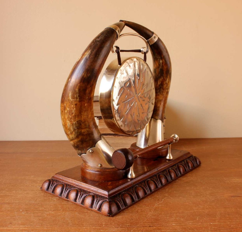A Victorian dinner gong featuring a hammered silver-plated disc suspended between two curved bovine horns mounted on a carved oak base with a striker. View VIII