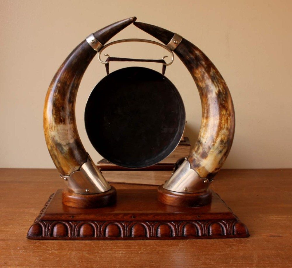 A Victorian dinner gong featuring a hammered silver-plated disc suspended between two curved bovine horns mounted on a carved oak base with a striker. View X