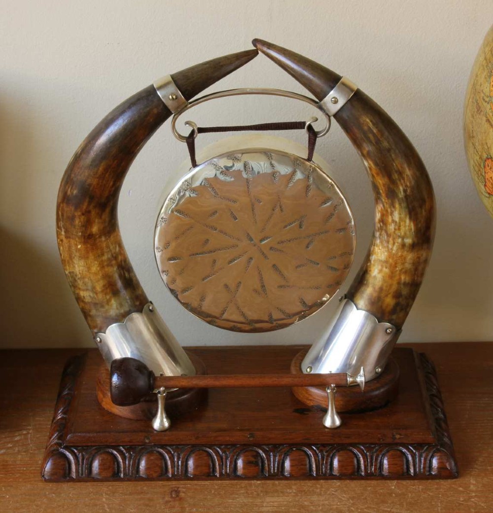 A Victorian dinner gong featuring a hammered silver-plated disc suspended between two curved bovine horns mounted on a carved oak base with a striker. View XI