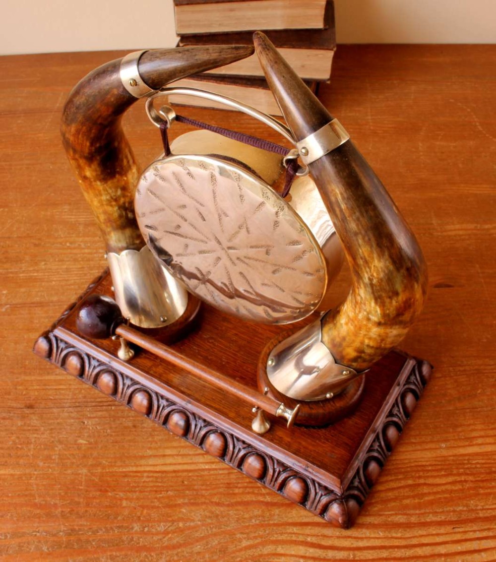 A Victorian dinner gong featuring a hammered silver-plated disc suspended between two curved bovine horns mounted on a carved oak base with a striker. View XII