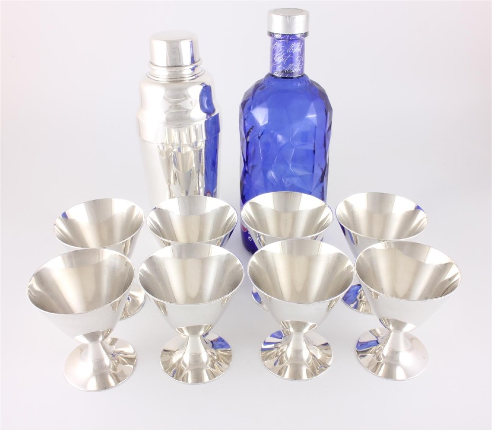 A silver-plated Art Deco cocktail shaker accompanied by eight matching conical goblet glasses arranged on a white background. View II