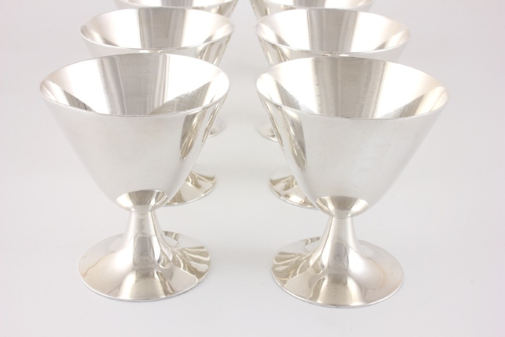 A silver-plated Art Deco cocktail shaker accompanied by eight matching conical goblet glasses arranged on a white background. View IV