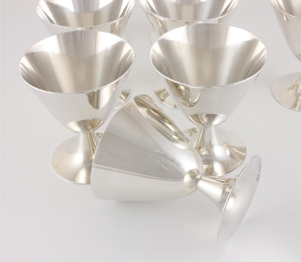 A silver-plated Art Deco cocktail shaker accompanied by eight matching conical goblet glasses arranged on a white background. View VII
