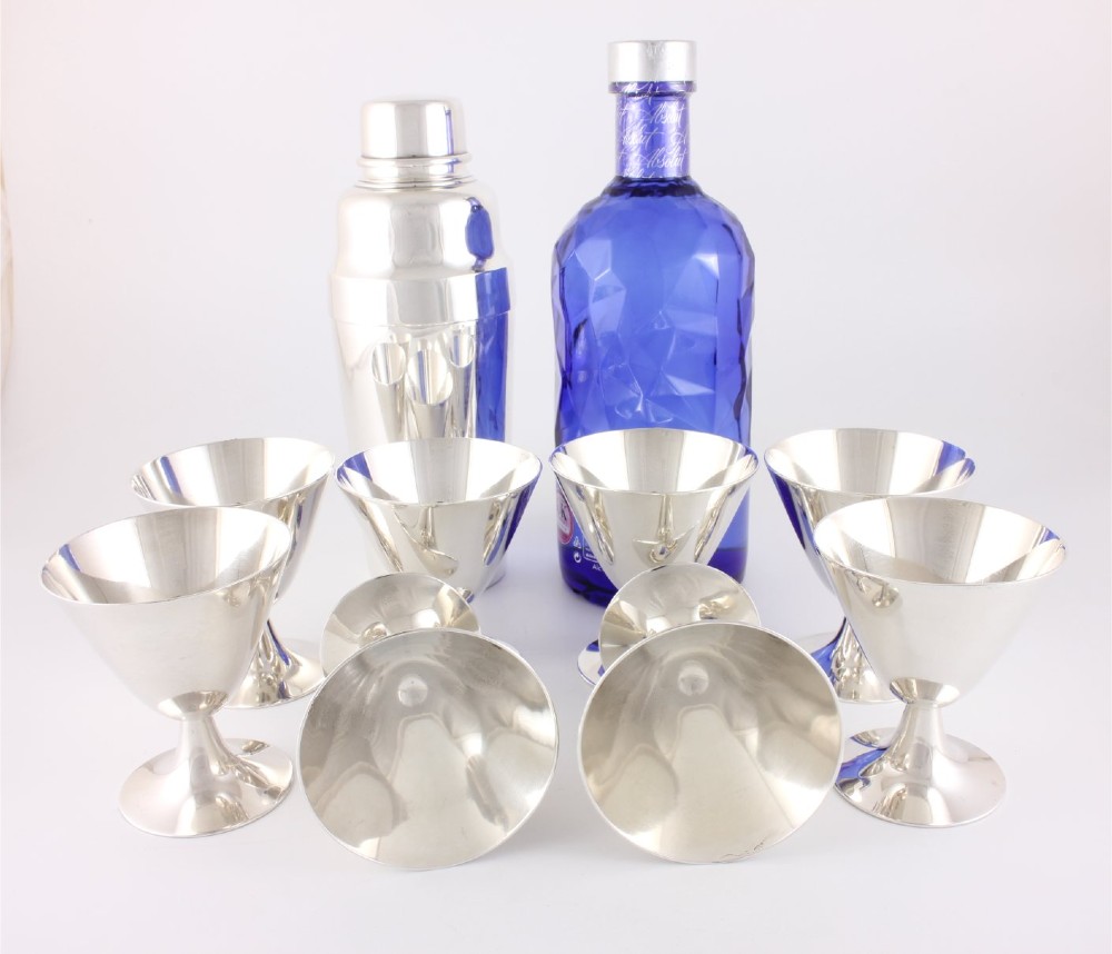 A silver-plated Art Deco cocktail shaker accompanied by eight matching conical goblet glasses arranged on a white background. View VIII
