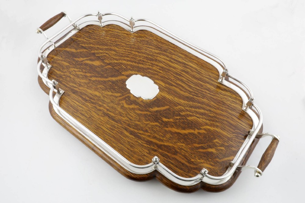 A late Victorian shaped English oak serving tray featuring a silver-plated raised gallery rail, twin wood-mounted handles, and a central blank silver cartouche.