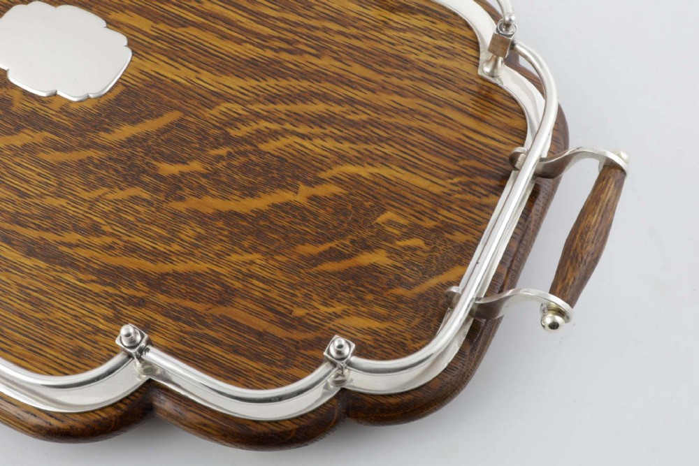 A late Victorian shaped English oak serving tray featuring a silver-plated raised gallery rail, twin wood-mounted handles, and a central blank silver cartouche. View V