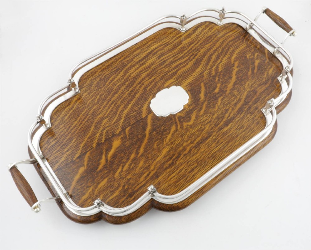 A late Victorian shaped English oak serving tray featuring a silver-plated raised gallery rail, twin wood-mounted handles, and a central blank silver cartouche. View VI