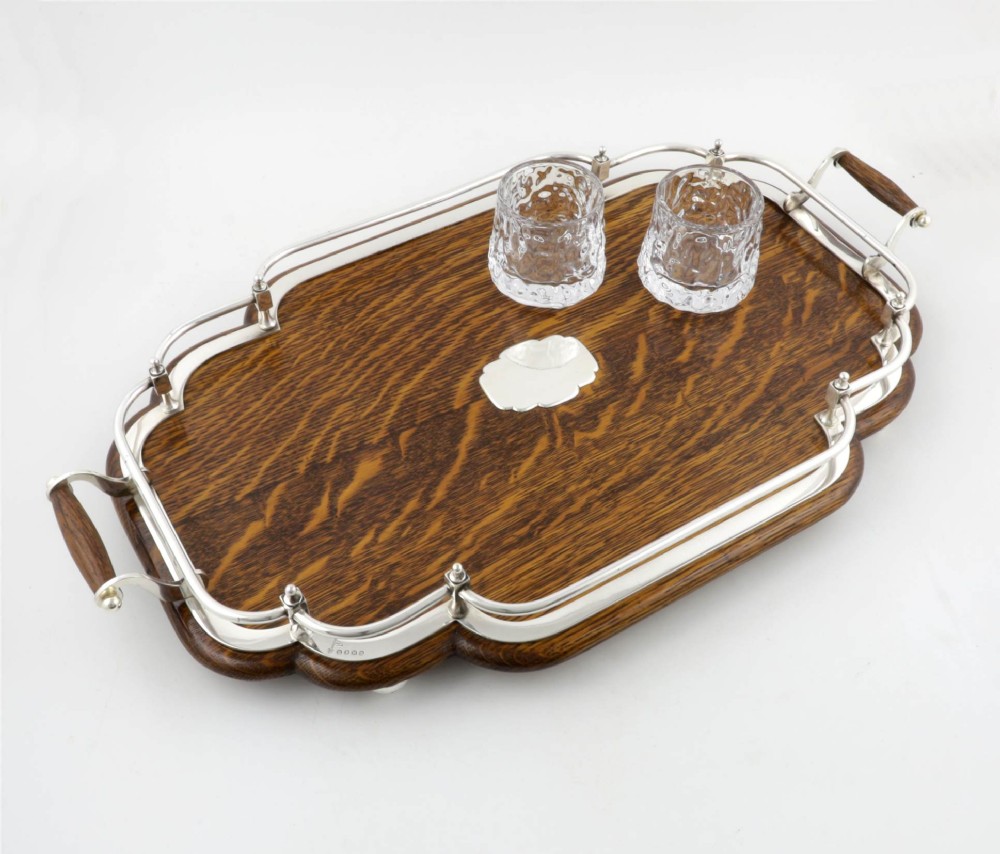 A late Victorian shaped English oak serving tray featuring a silver-plated raised gallery rail, twin wood-mounted handles, and a central blank silver cartouche. View X